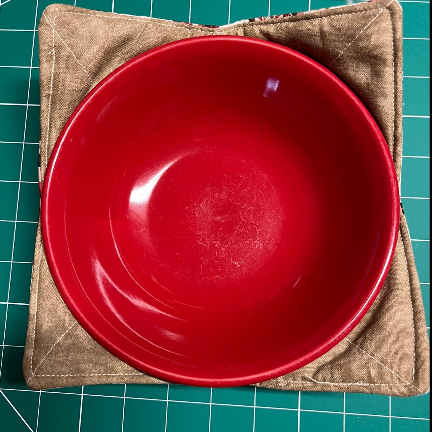 A red ceramic bowl in a cotton bowl cozy sitting on a green cutting mat.