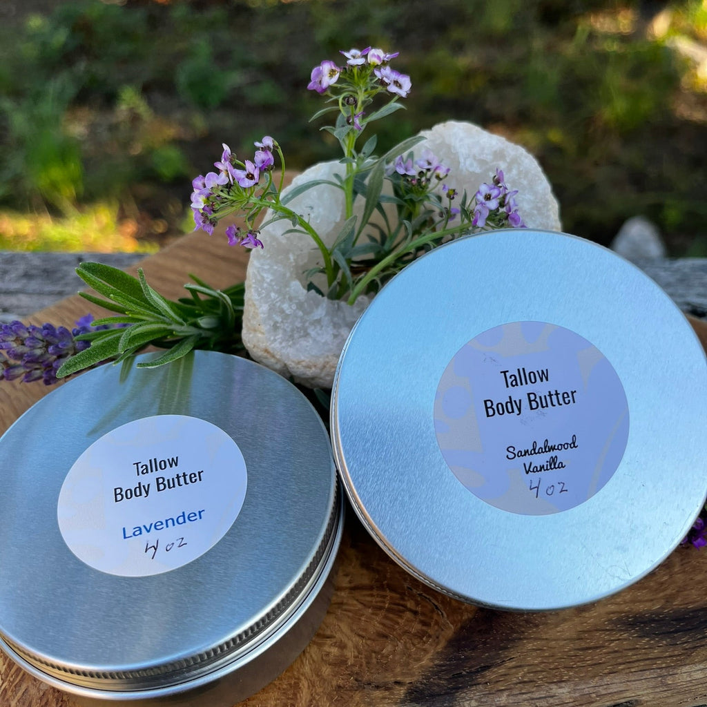 Two round tins of tallow body butter one lavender and one sandalwood vanilla on a wooden board.