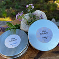 Two round tins of tallow body butter one lavender and one sandalwood vanilla on a wooden board.